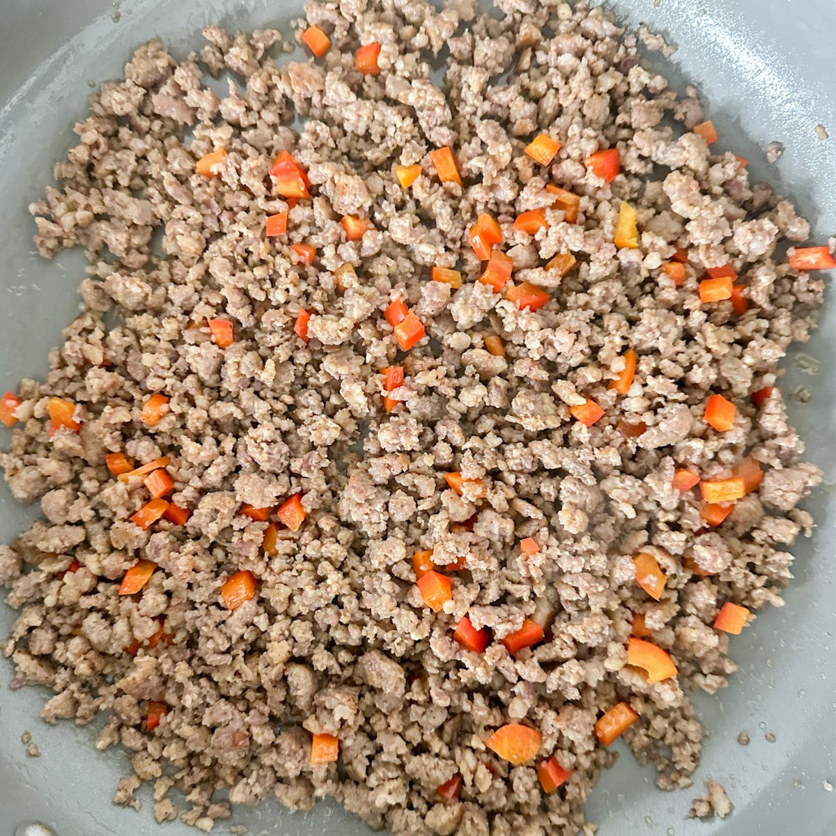 Skillet with cooked sausage and red peppers.